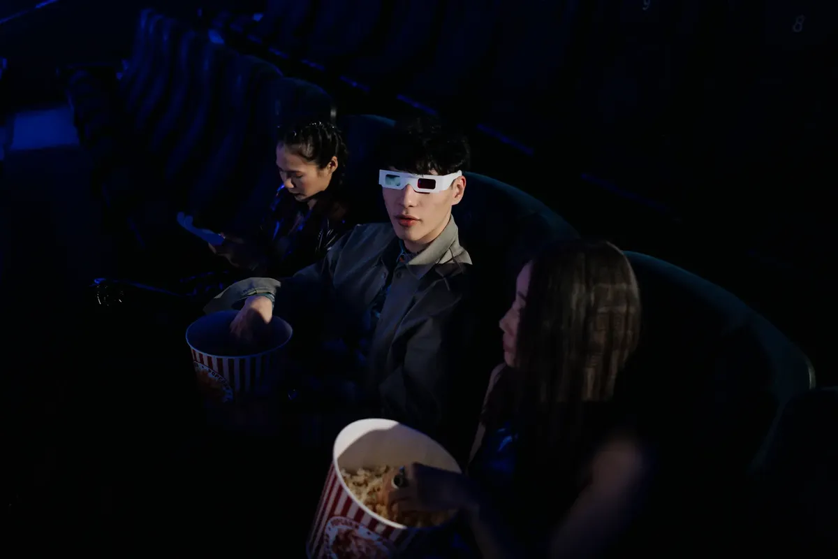 A group of young adults watching a 3D movie at a cinema, enjoying popcorn.