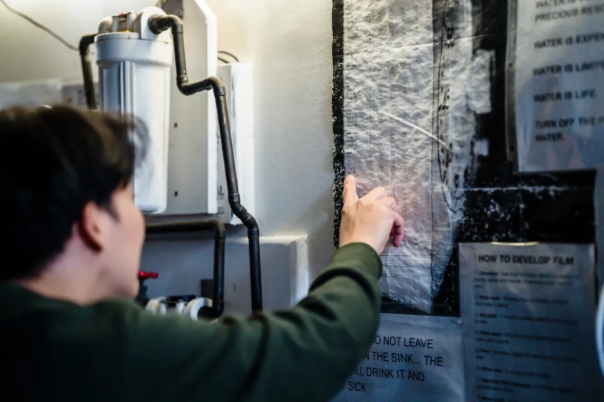 A man pointing at a film development guide on a wall in a workshop setting.