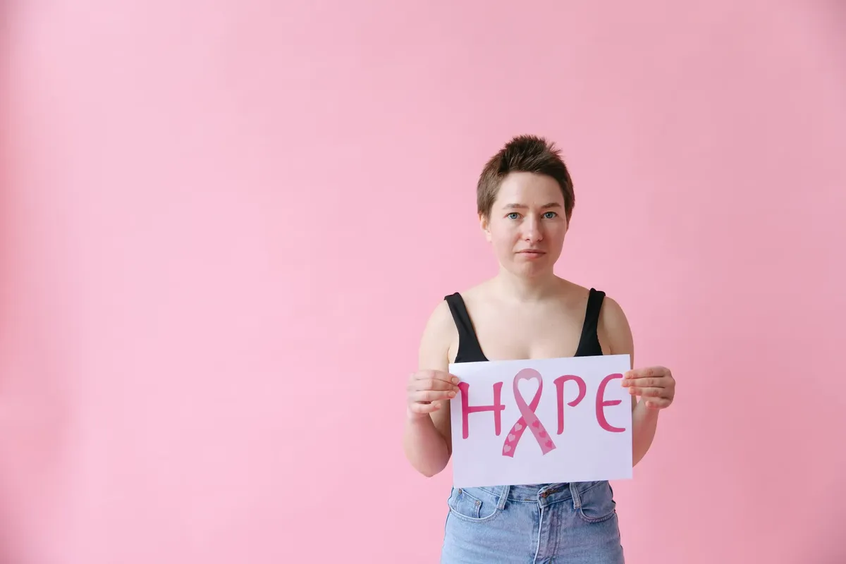 Woman holding a pink ribbon hope sign on pink background, symbolizing breast cancer awareness.