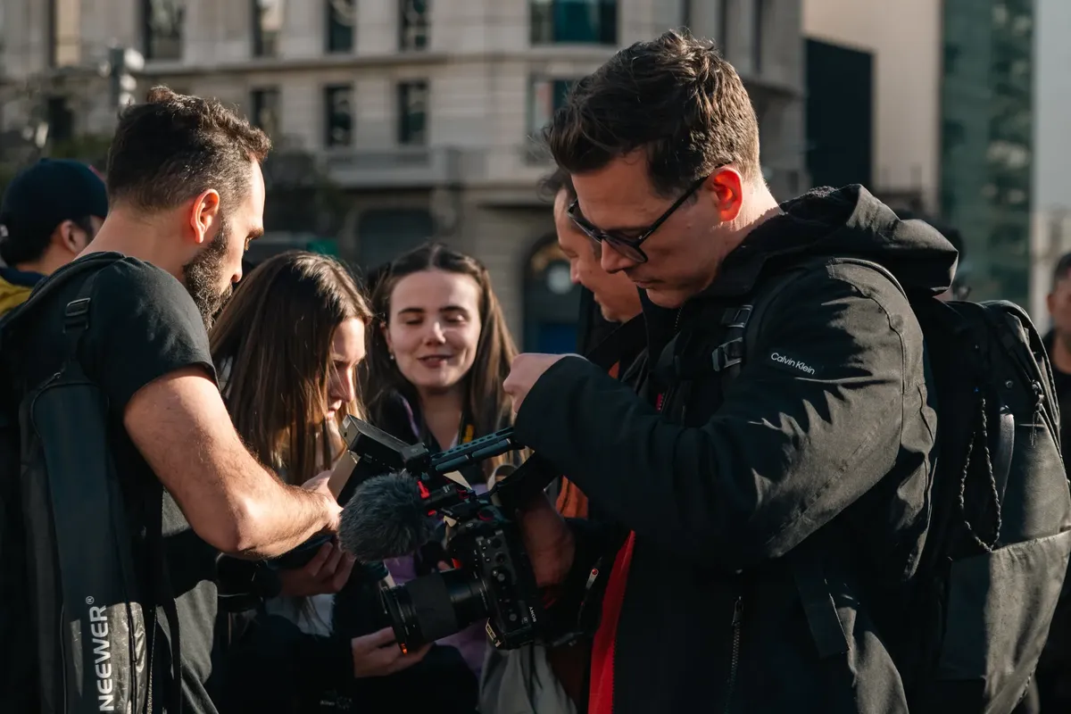 A diverse group of filmmakers collaborates outdoors, reviewing footage on a professional camera.