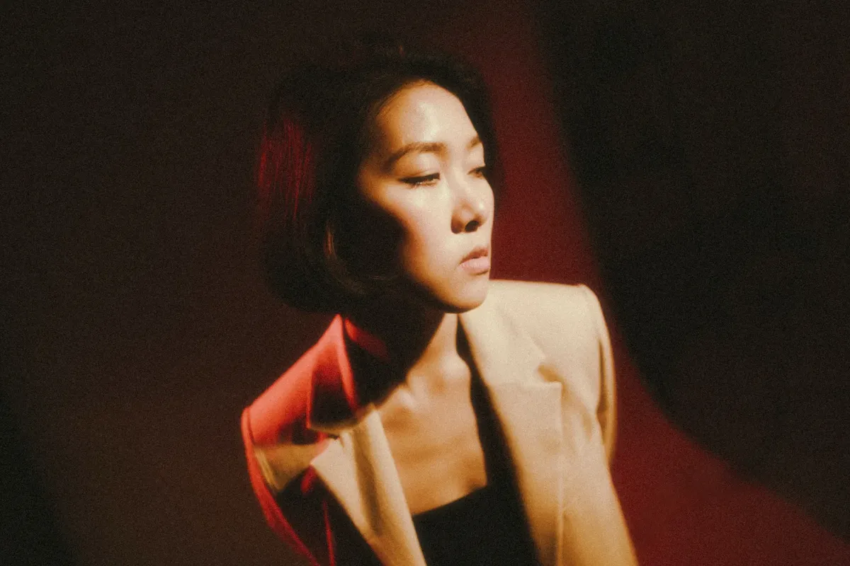 Portrait of a pensive woman in a beige jacket with artistic lighting casting shadows.