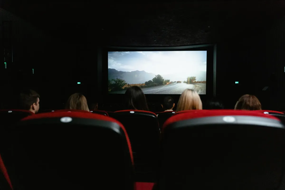 大きなスクリーンと赤い座席の劇場で映画を観ている人々の後方からの様子。
