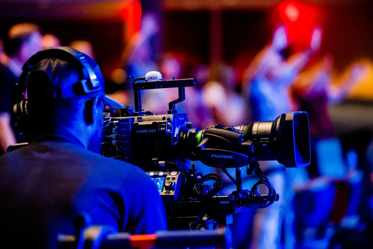 A cameraman using professional video equipment to film an event indoors.