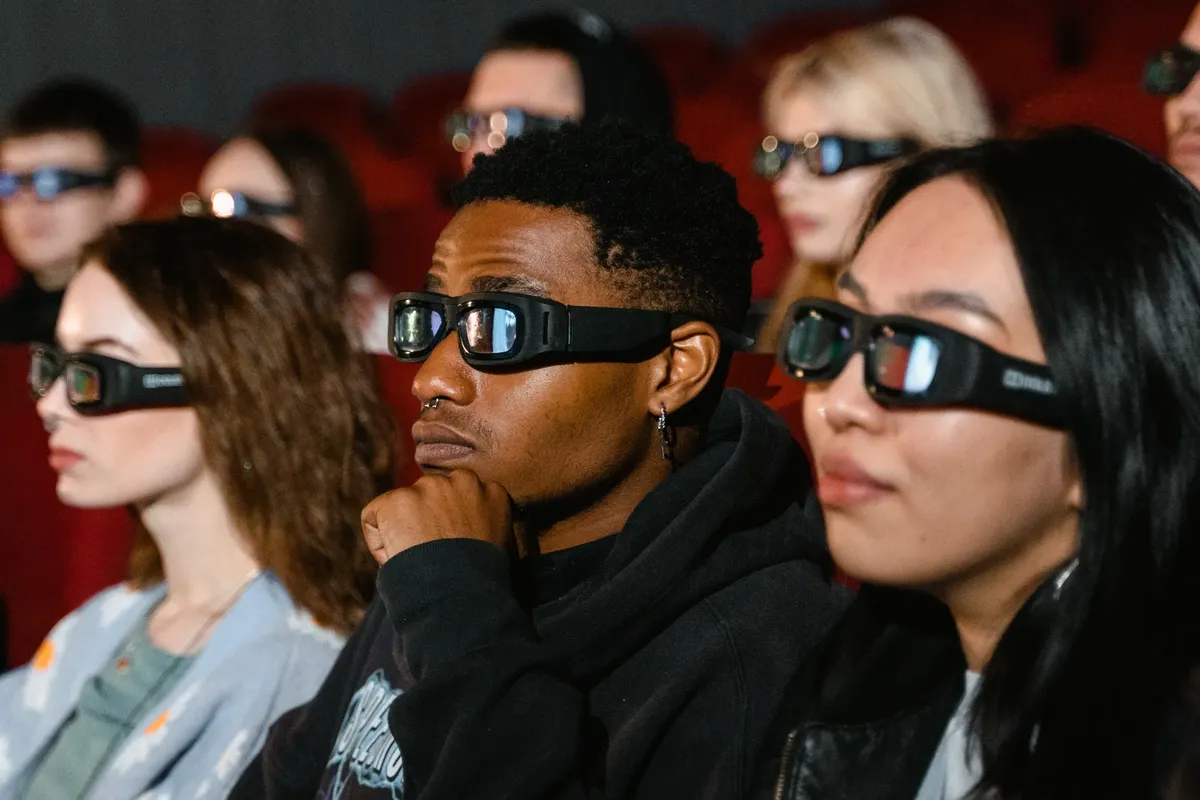 A diverse group of adults wearing 3D glasses are watching a movie in a cinema theater.