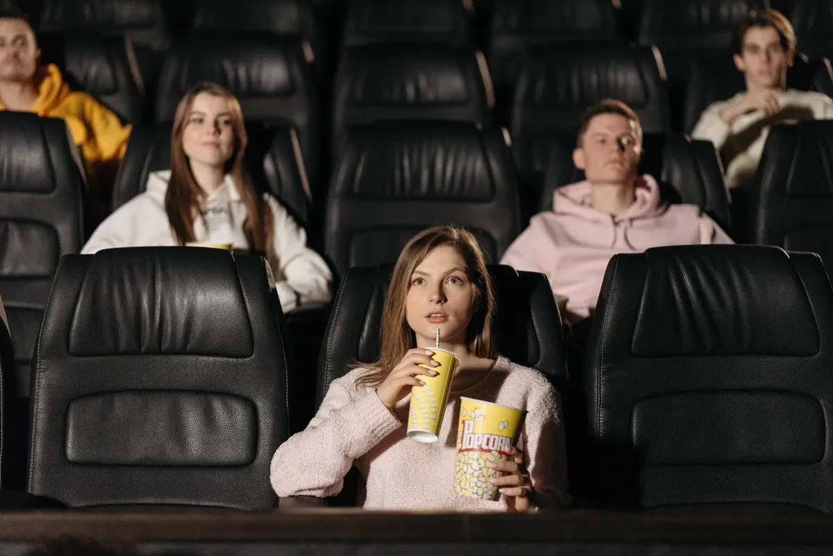 Group of young adults watching movie in theater with popcorn and drinks.