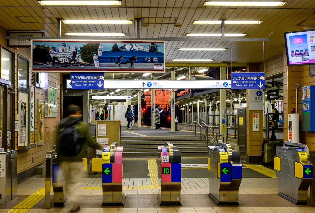混雑した夜の日本の電車駅で、切符ゲートと乗客がプラットフォームエリアに進んでいる様子。