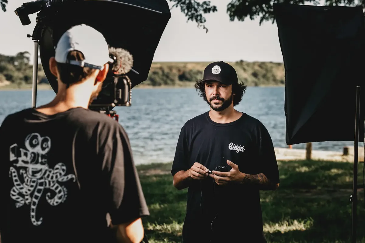 Male colleagues with video camera and walkie talkie standing on coast of pond while shooting film