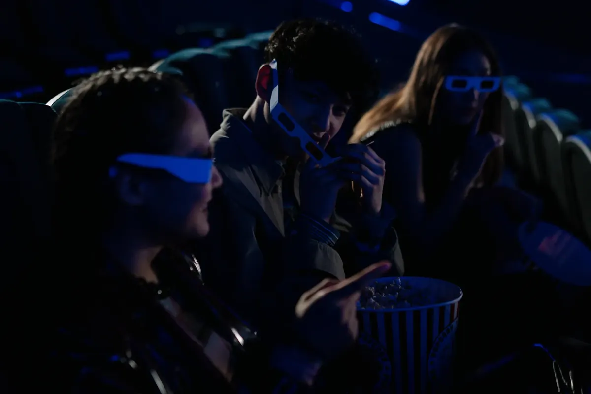 Friends wearing 3D glasses enjoy popcorn and movies in a cinema theater.