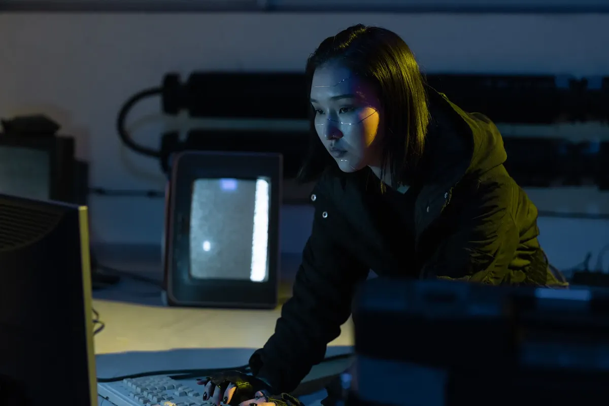 一名女子在昏暗房間裡打鍵盤，周圍有科技設備。