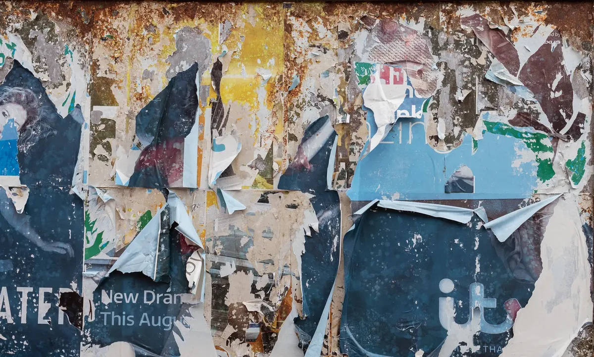 A close-up of layered, torn posters on a rusty notice board, showcasing urban decay.