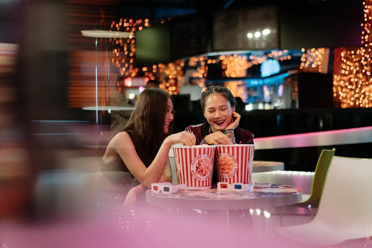 Two friends enjoying popcorn and bonding in a vibrant cinema setting.