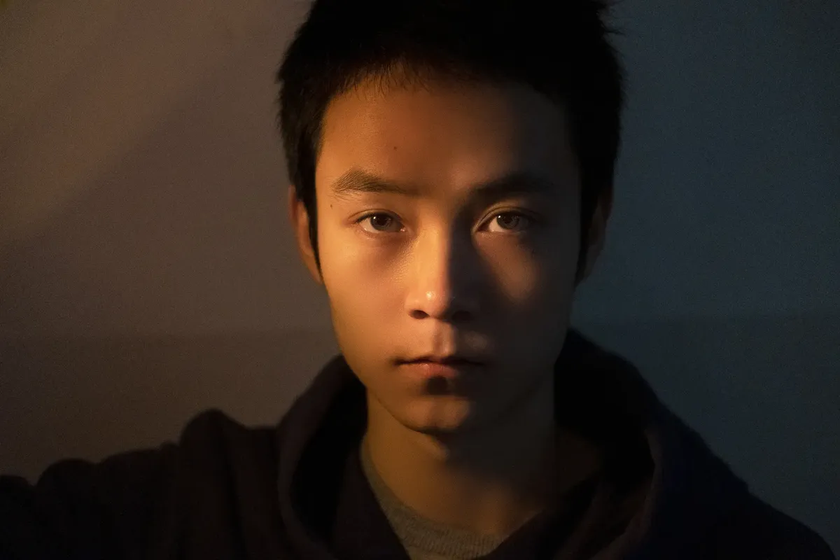 Close-up portrait of a young Asian man with warm moody lighting and a serious expression.