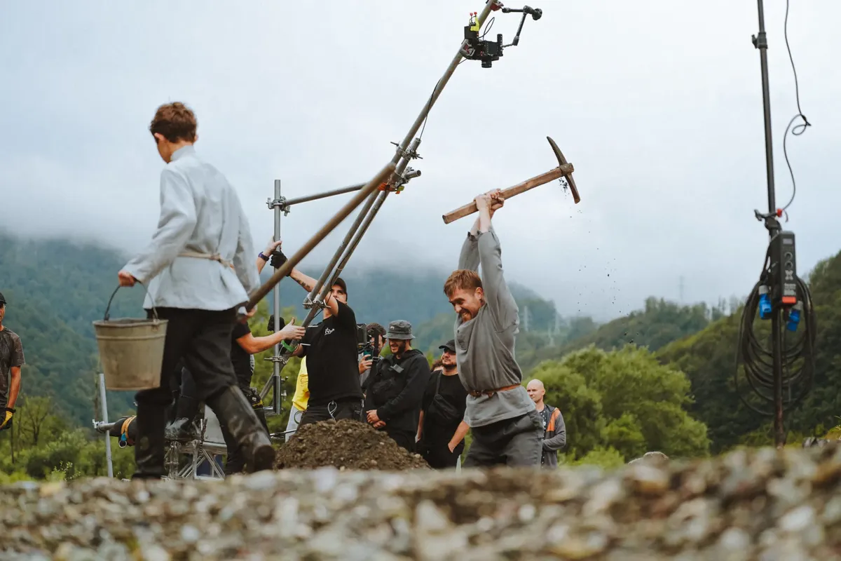 Film crew setting up a historical scene with actors outdoors in nature.