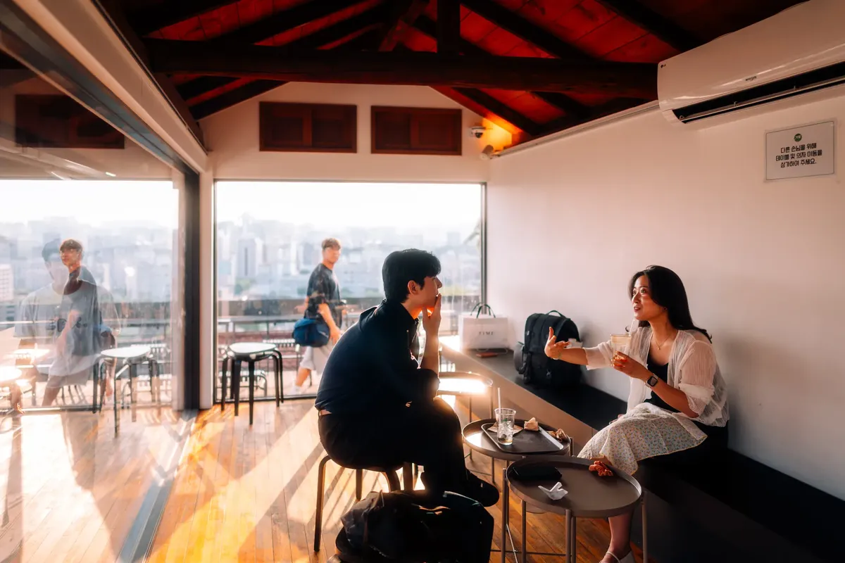 People enjoying a casual chat in a Seoul café with city skyline visible, creating a relaxed atmosphere.