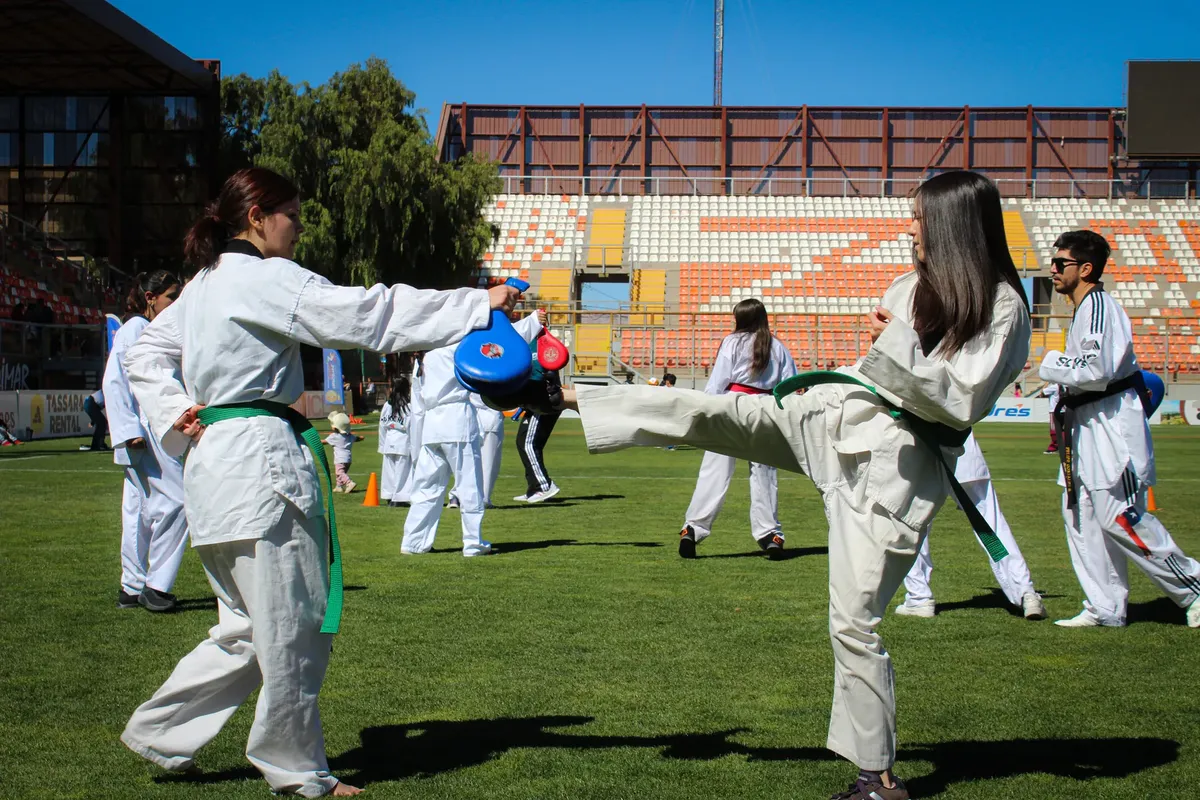 Group practicing martial arts outdoors in a stadium with focus on two women sparring.