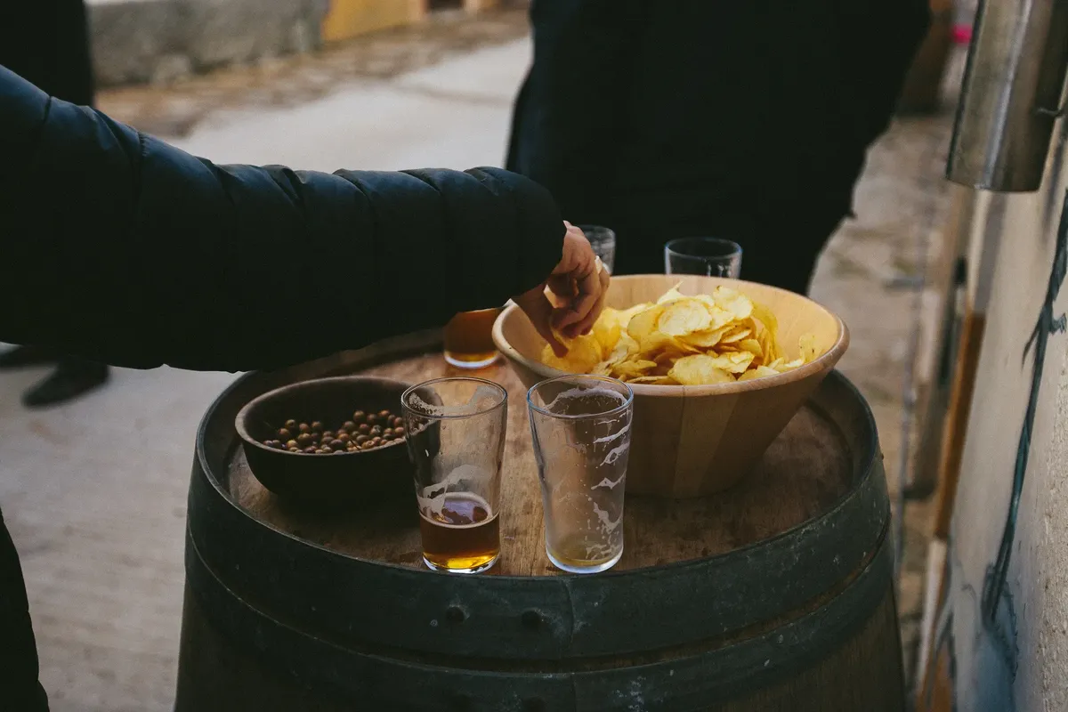 An outdoor gathering with beer, potato chips, and nuts on a barrel. Ideal for social event themes.