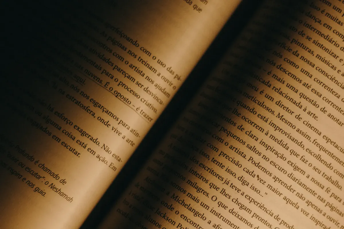 Close-up of old book pages with warm lighting, showcasing yellowed paper and Portuguese text.