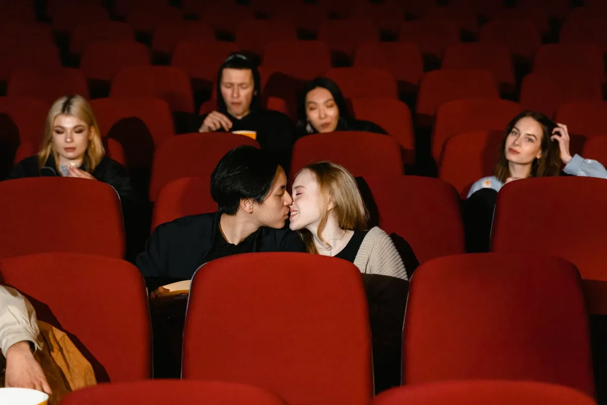 A couple kisses in a cozy movie theater setting among other moviegoers.