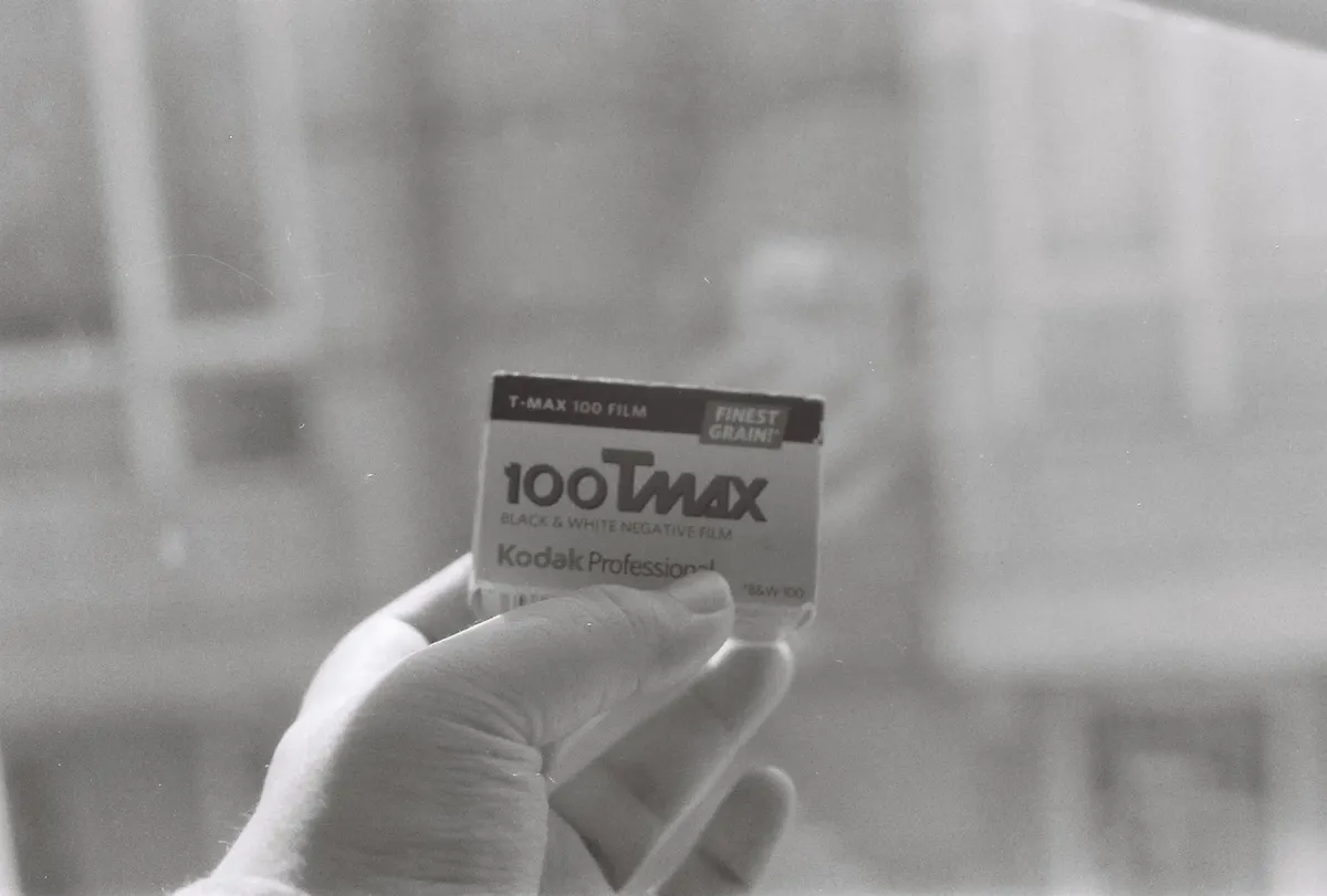 손에 쥔 키오스크 T-Max 100 블랙앤화이트 필름의 세부 모습을 보여주는 베이직한 사진 장비.