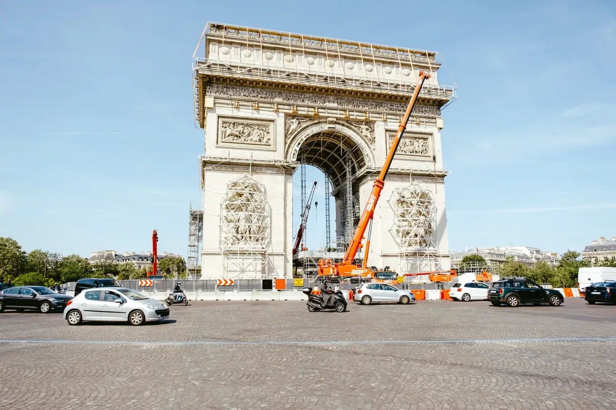 The Arc de Triomphe in Paris undergoing construction and maintenance with visible traffic around.