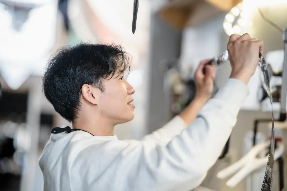 アジアの男性フォトグラファーが暗室の中でフィルムを開発している。詳細と技術に焦点を当てている。