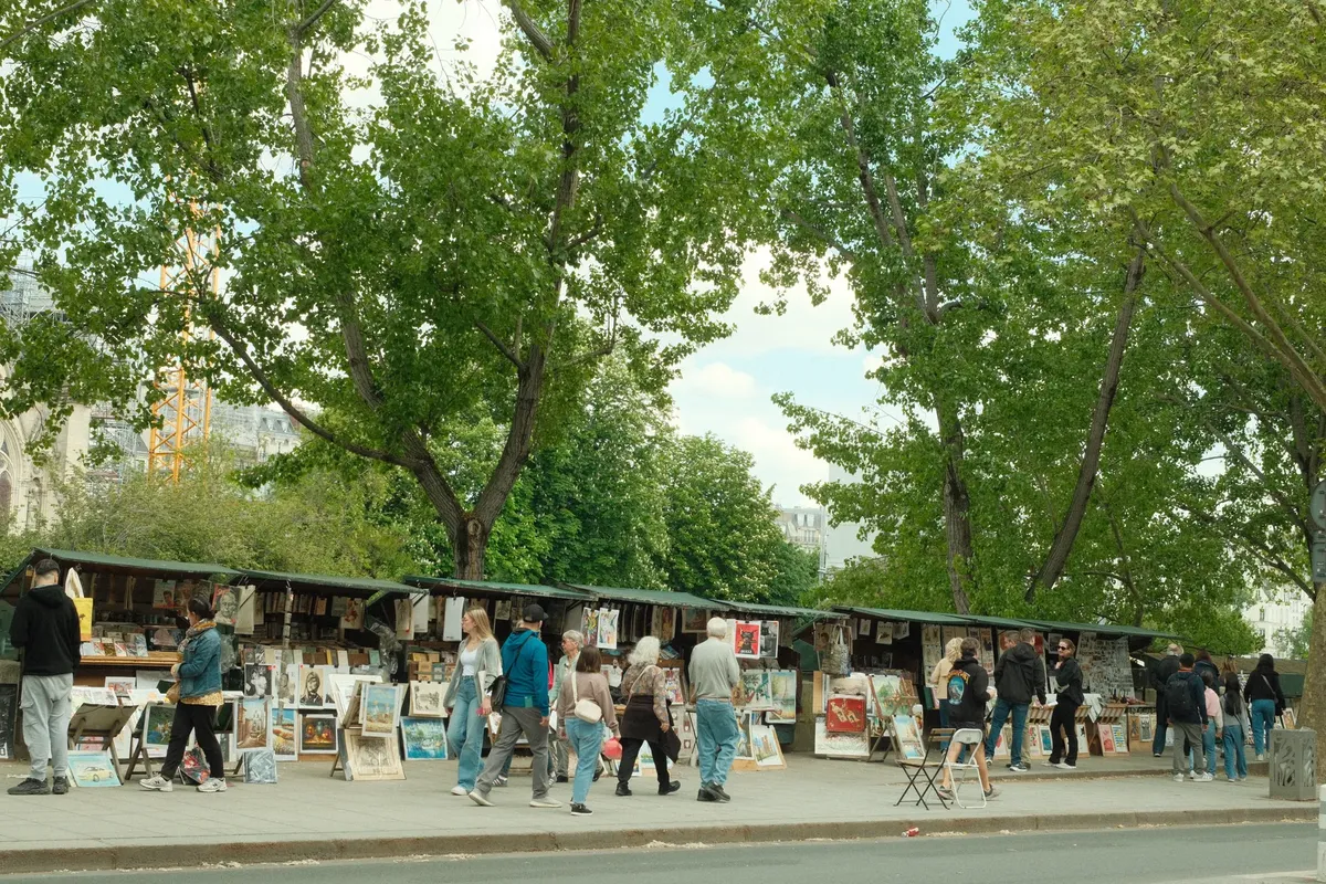 パリの街角に広がる色鮮やかなアートマーケット。観光客が作品を探索している姿。
