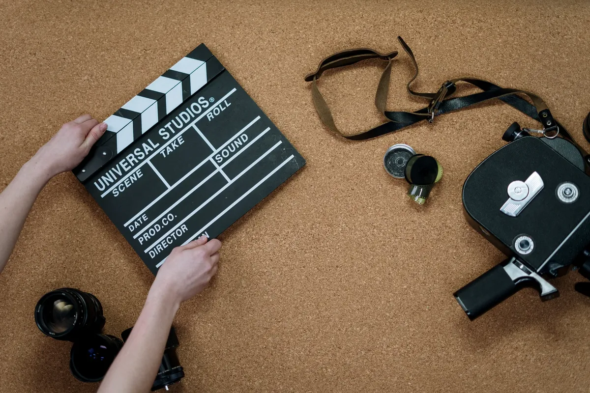 Top view of classic filmmaking tools including a slate and vintage camera on a cork surface.