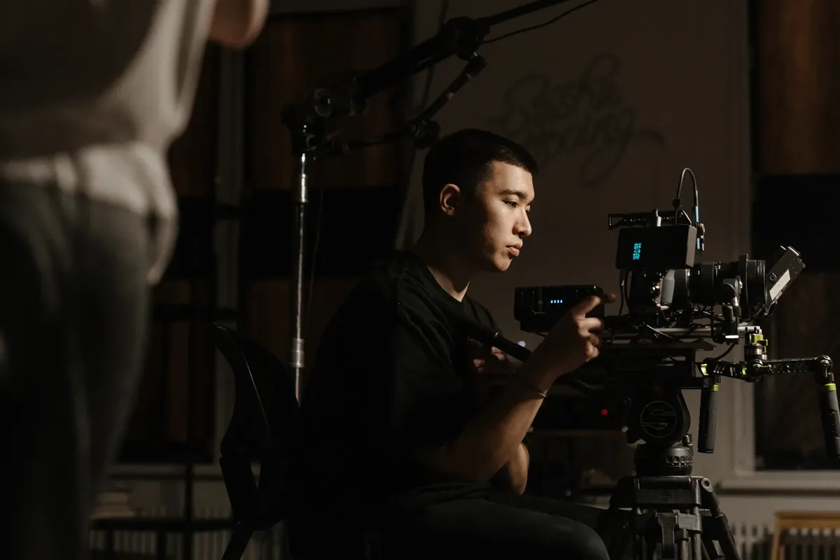 Side view of cameraman operating professional equipment during film production indoors.