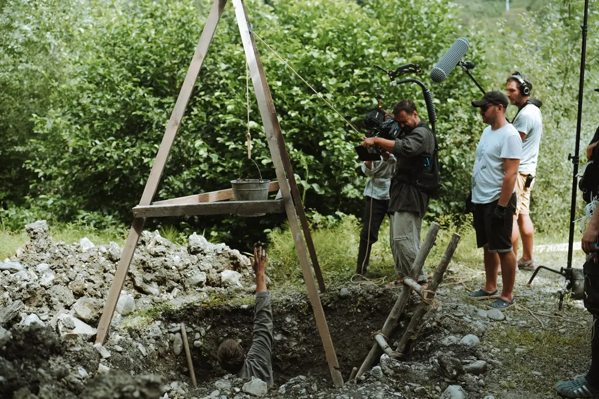 Film crew with camera and sound equipment shooting a scene outdoors in a rural setting.