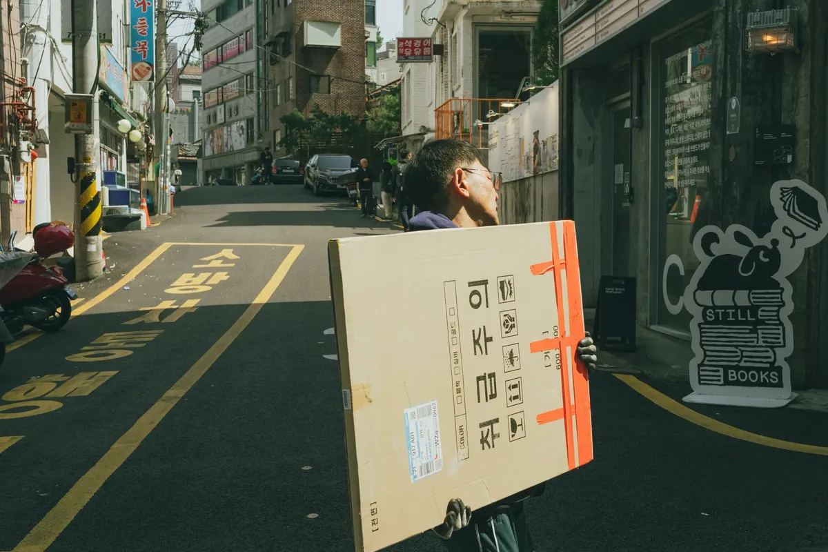 A man carries a large package on a vibrant Seoul street, showcasing urban life in South Korea.
