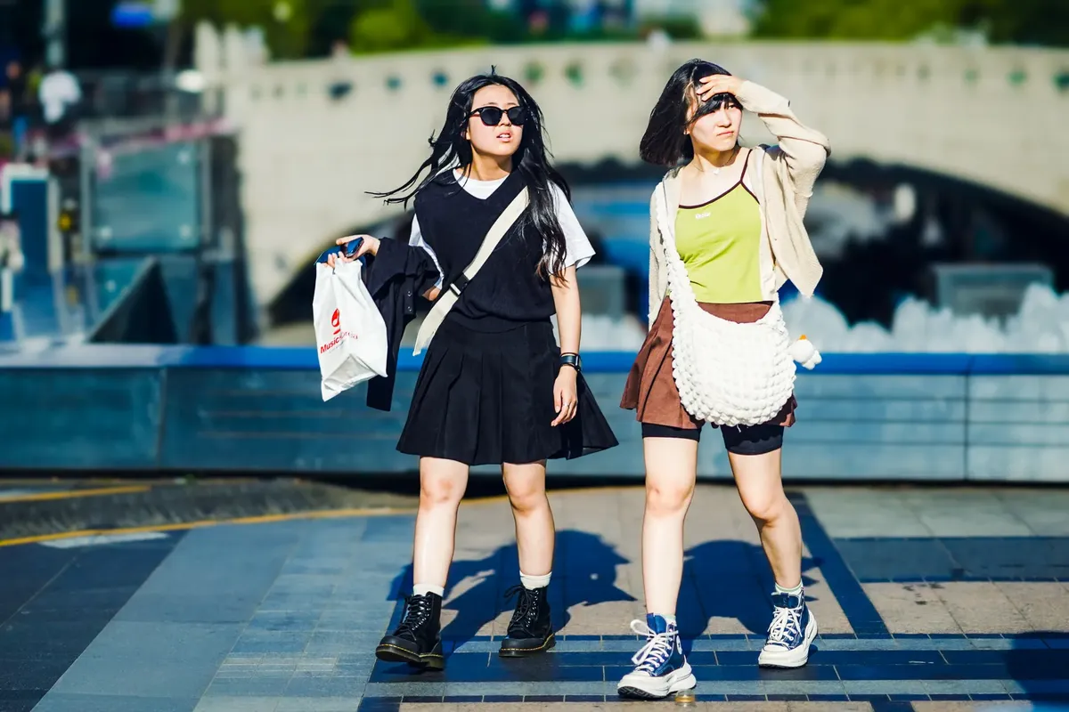 Two young women walk through Seoul on a sunny day, showcasing urban fashion.