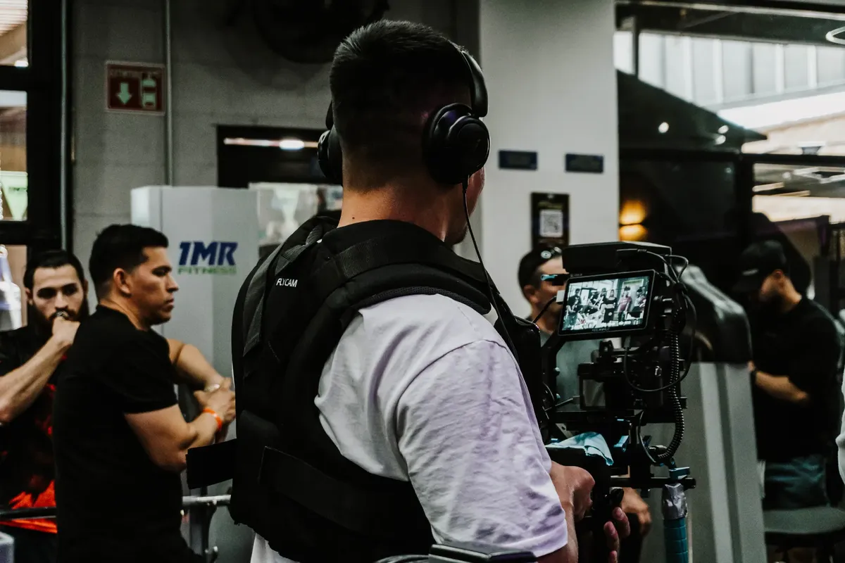Back view of a filmmaker using a camera rig indoors with a focus on capturing event activities.