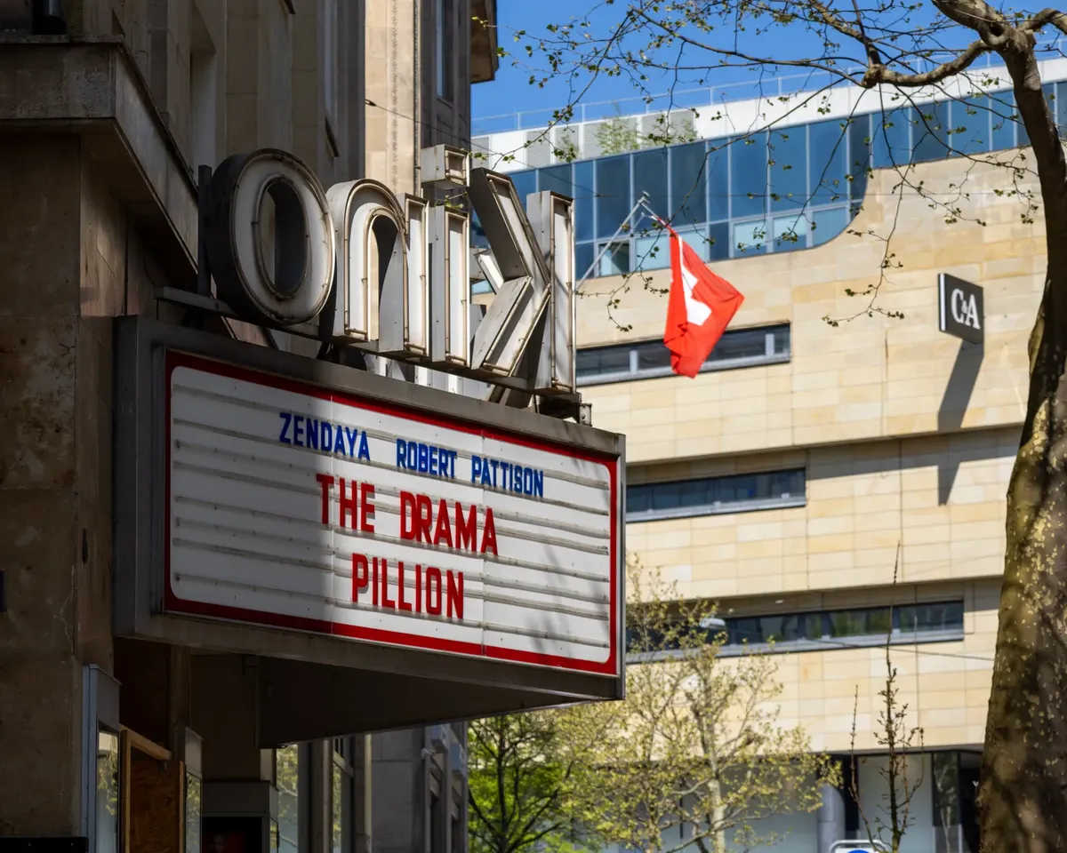 Cinema marquee displaying movie title in urban setting with Swiss flag nearby.