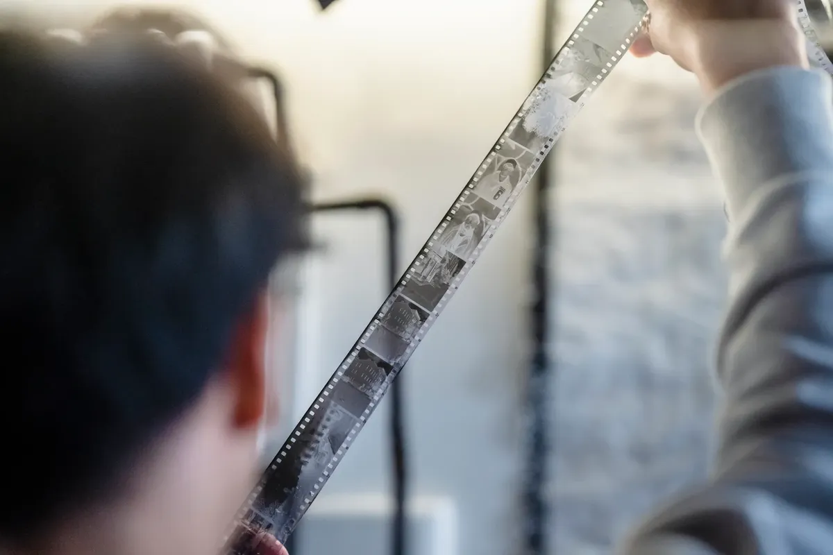 Adult examining a film strip indoors with focused attention on details and imagery.