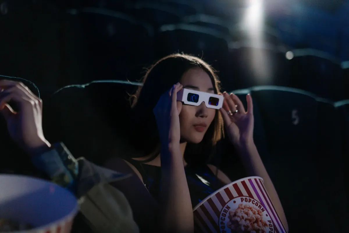Asian woman wearing 3D glasses, enjoying popcorn in a movie theater.
