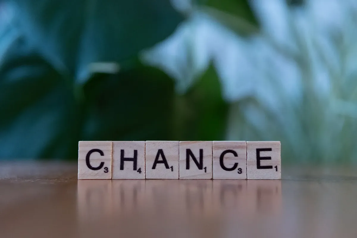 Scrabble tiles spelling 'chance' on a wooden surface with a blurred green background.